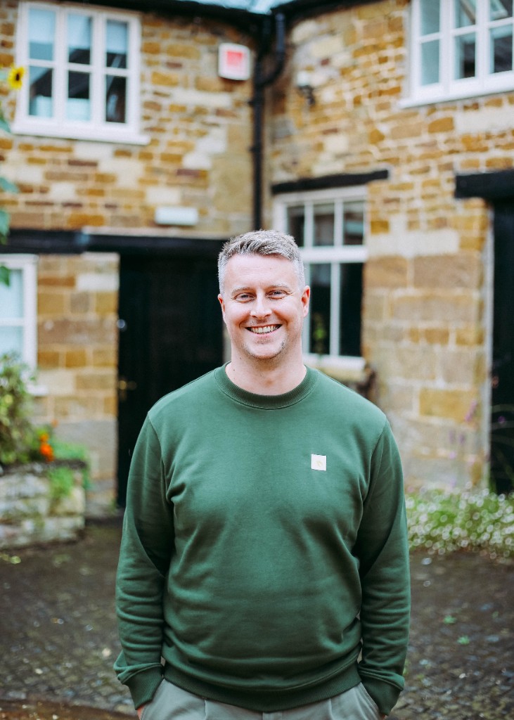 Ben smiling outdoors in front of a traditional stone building